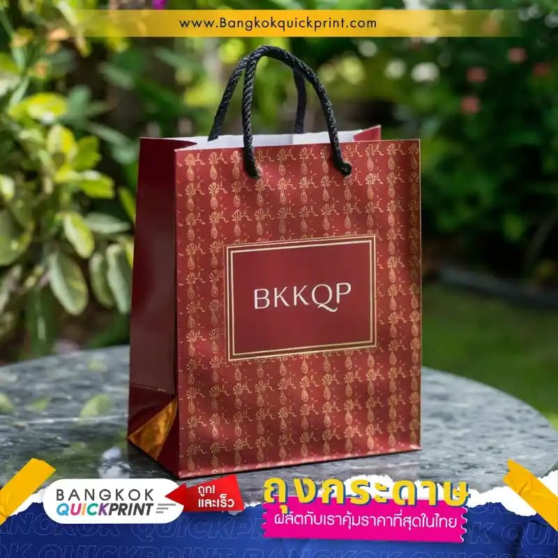 ถุงกระดาษสีแดงเคลือบลามิเนตเงา พร้อมสกรีนลายและแบรนด์ BKKQP ด้วยปั๊มเคฟอยล์ทอง ใช้หูหิ้วเชือกเกลียวสีดำ