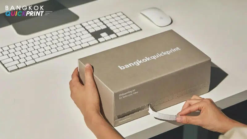 มือกำลังดึงแถบเปิดกล่องพัสดุแบบฉีกง่าย โลโก้ bangkokquickprint บนฝากล่อง
